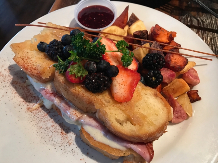 A photo of the KS Monte Cristo at Kitchen Story in San Francisco, California. The sandwich is made with meyer lemon French toast, tasty smoked ham, Swiss cheese and served with a spicy raspberry jam and rainbow potatoes on the side.