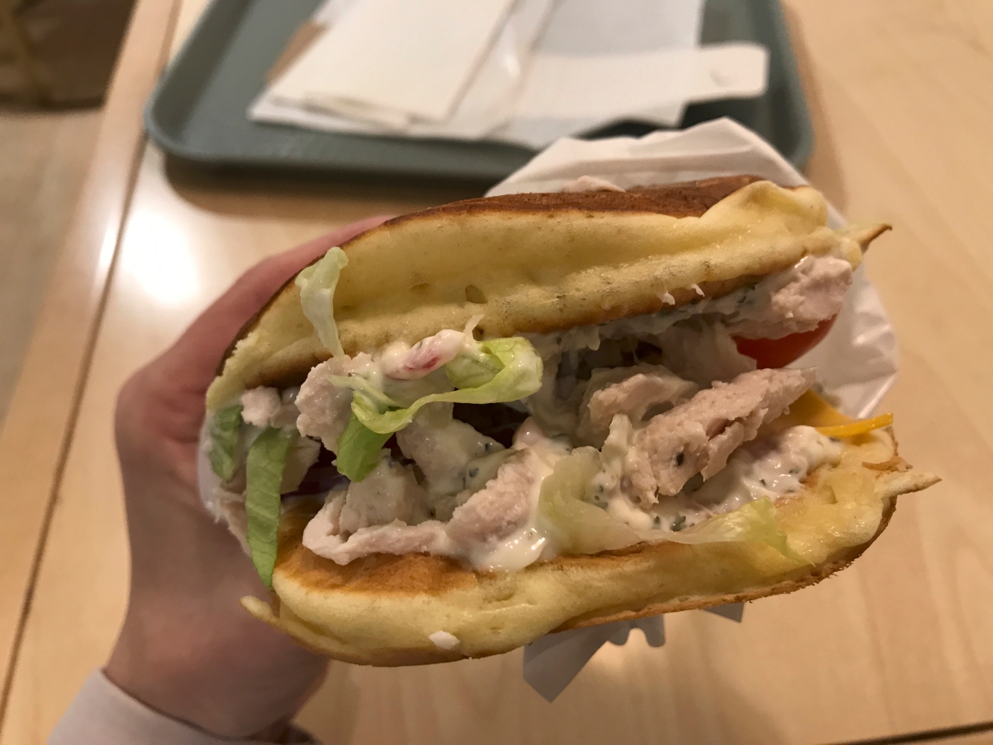 A photo of a hand holding a chicken pancake burger from breakfast and lunch fast food joint Pancs in Lausanne, Switzerland. Is it technically breakfast, lunch or dinner? Weird and strange, but good! Photo Courtesy of FoodWaterShoes