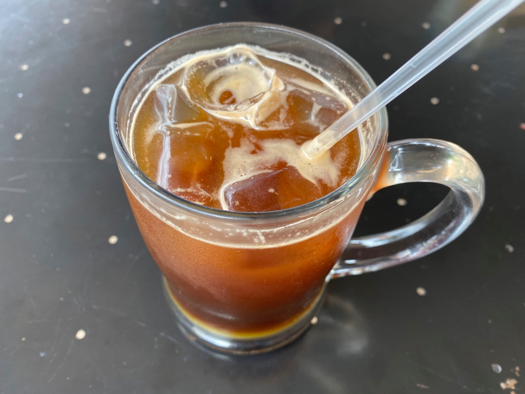 A photo of a seasonal coffee drink known as the pink and bold cold brew at Question Coffee, a cute cafe in Kigali, Rwanda. The drink is made with 18 hour cold brew coffee, passion fruit and tree tomato syrup, a hint of brown spiced syrup and fresh local dairy milk served in a frosty cold mug. Photo Courtesy of FoodWaterShoes